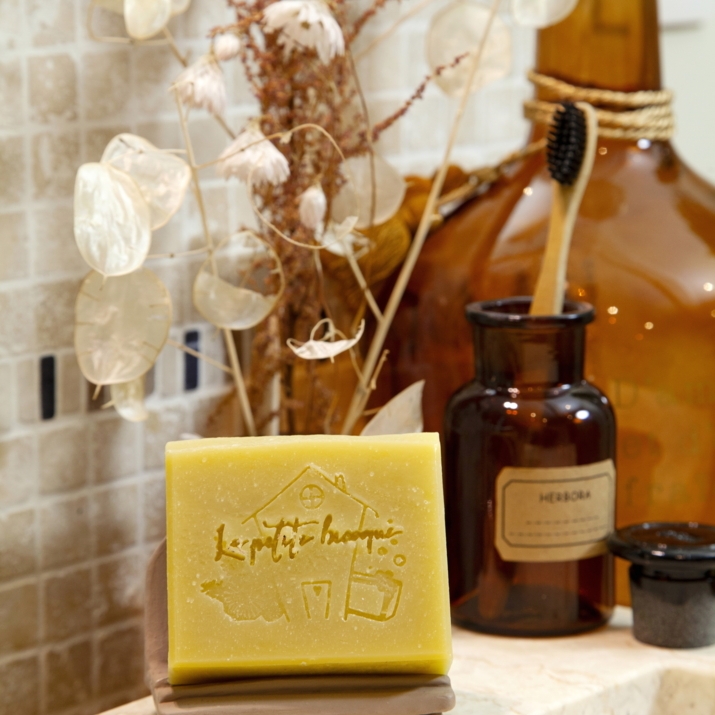 Savon estampillé du logo maison posé près de fleurs séchées et de flacons ambrés